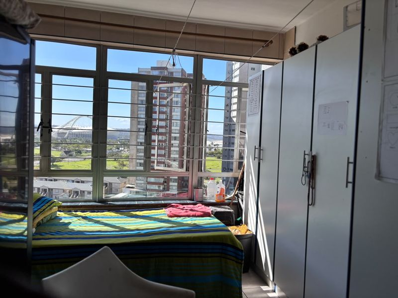 A bedroom featuring built-in cupboards, tiled flooring, and large windows offering an expansive urban and stadium view.