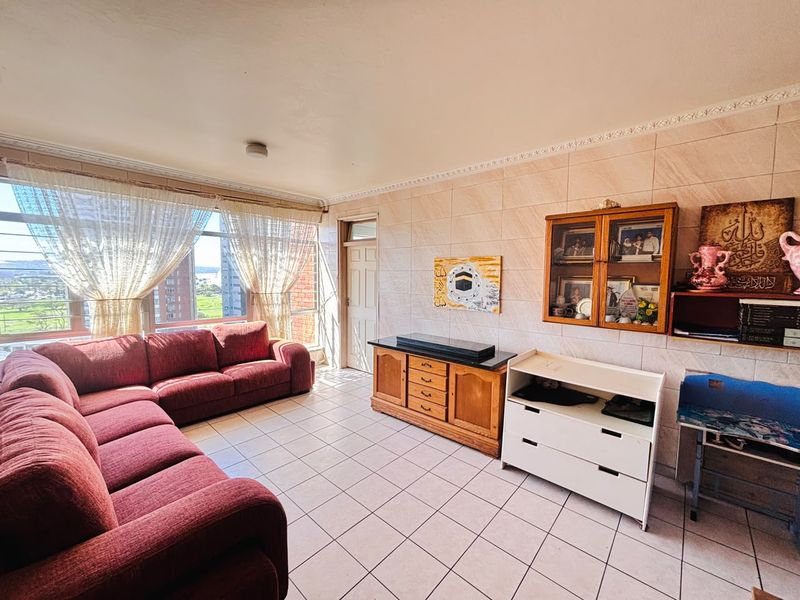 A spacious living room featuring ceramic floor tiles, tiled wall finishes, and large windows that provide ample natural light and views.