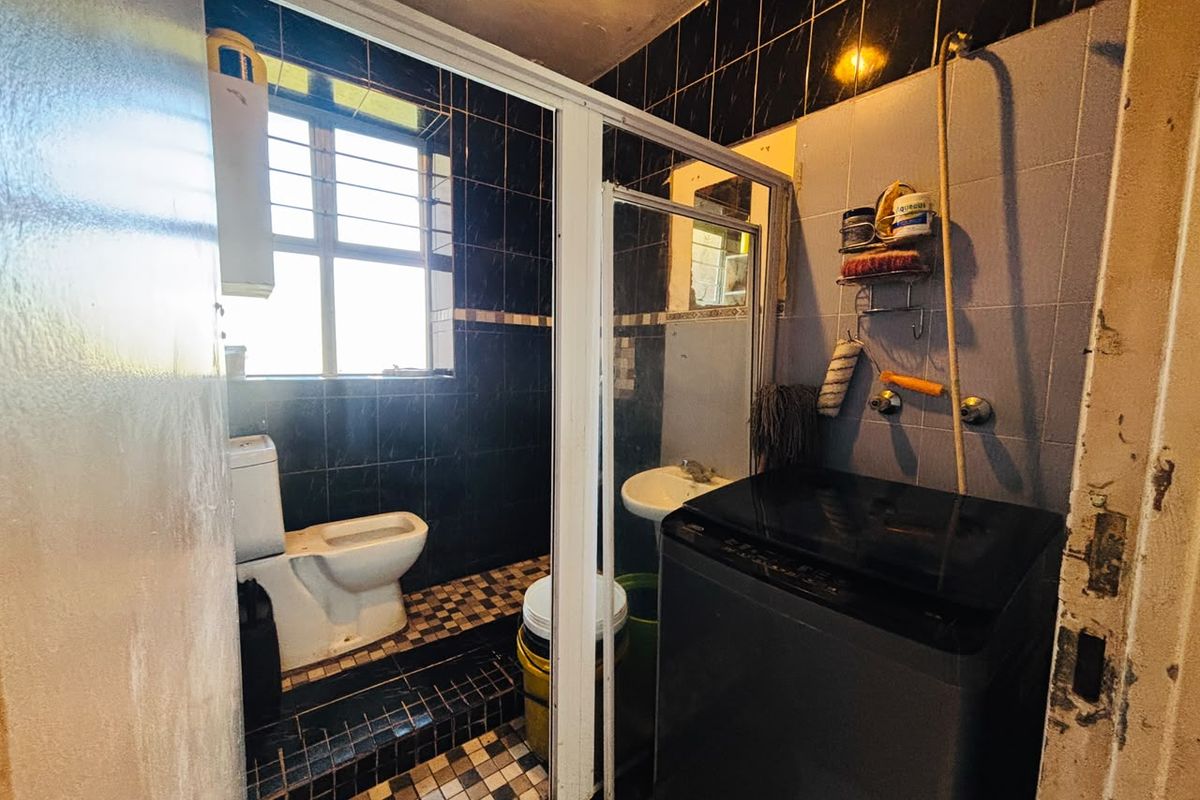 A compact bathroom featuring a toilet, washbasin, and shower enclosure with dark tiled walls and flooring, requiring cosmetic updates to improve its overall condition.