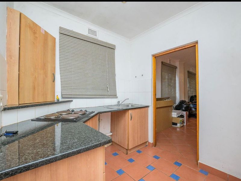 A functional kitchen featuring granite countertops, an electric hob, and built-in cabinetry, with tiled flooring and a tiled backsplash.
