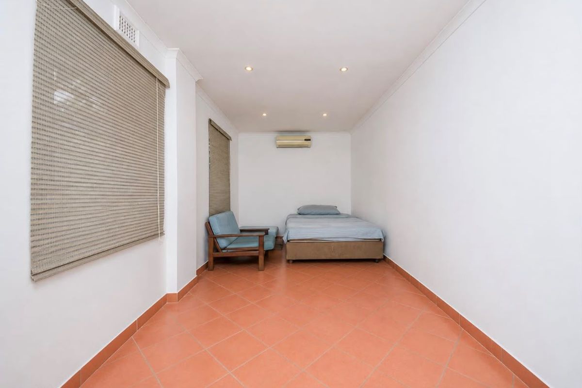 A simple bedroom featuring terracotta floor tiles, recessed downlighting, and a wall-mounted split-system air conditioner.