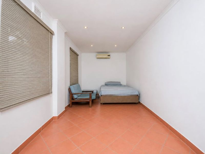 A simple bedroom featuring terracotta floor tiles, recessed downlighting, and a wall-mounted split-system air conditioner.