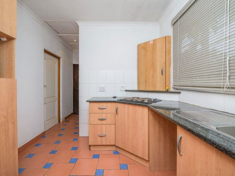 A functional kitchen featuring laminate cabinetry, granite countertops, a built-in hob, and a stainless steel sink with tiled backsplash.