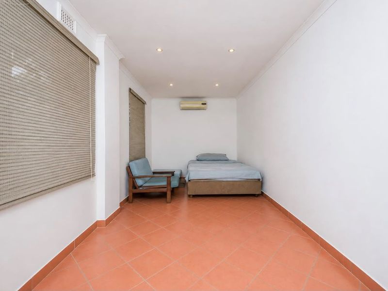 A simple bedroom featuring ceramic tiled flooring, recessed downlighting, and a wall-mounted split-system air conditioning unit.