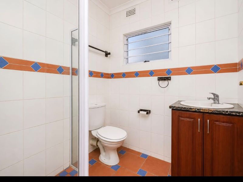 A functional bathroom featuring a vanity with granite countertop, a toilet, and a shower enclosure with dated decorative wall tiling.