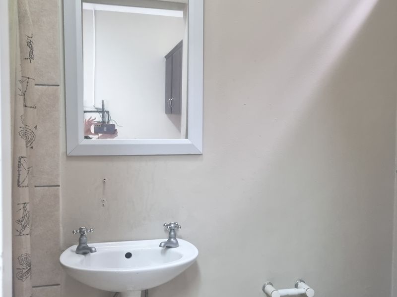 A basic bathroom featuring a wall-mounted basin, mirror, and tiled shower area, requiring cosmetic updates to improve its overall condition and appeal.