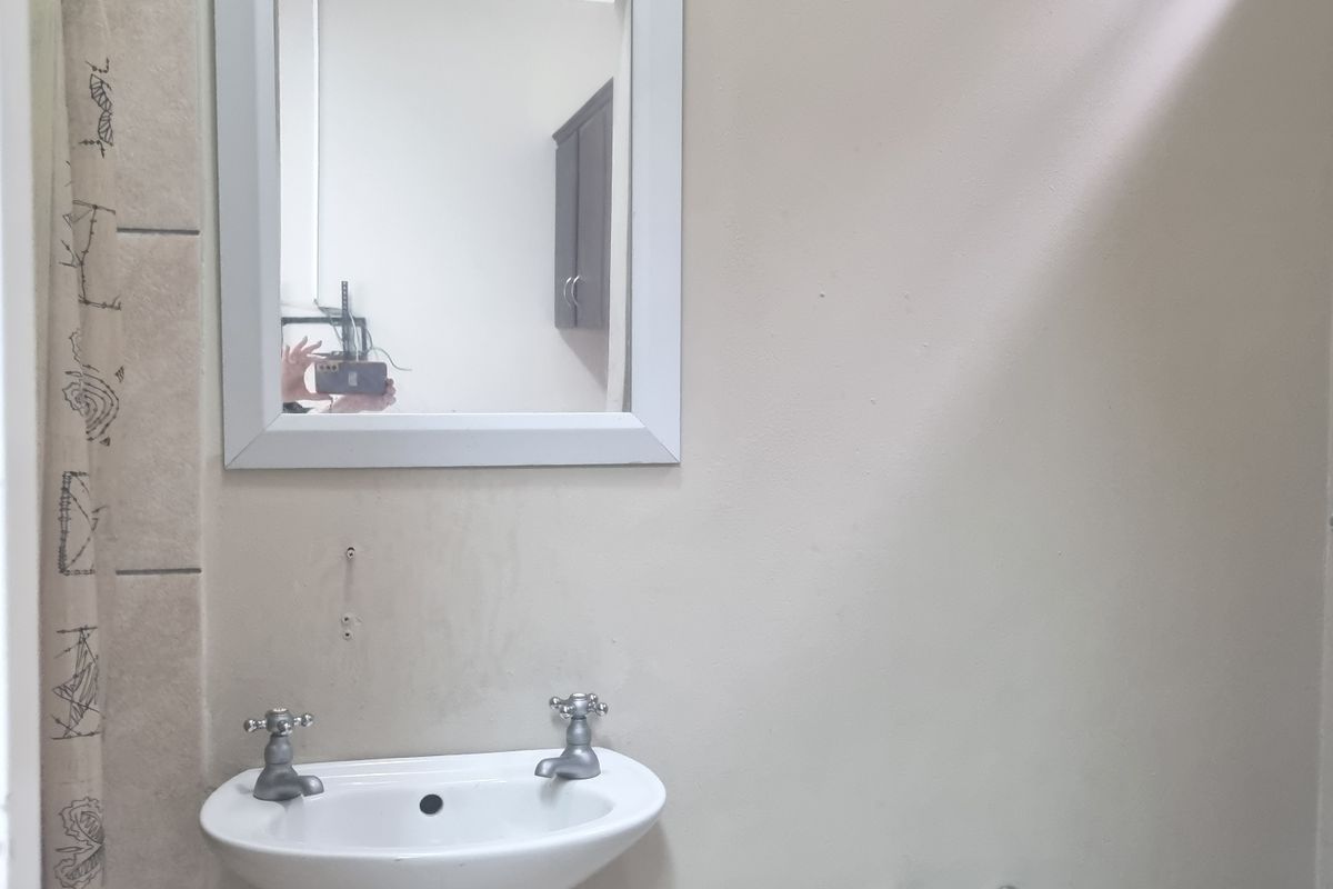 A basic bathroom featuring a wall-mounted basin, mirror, and tiled shower area, requiring cosmetic updates to improve its overall condition and appeal.