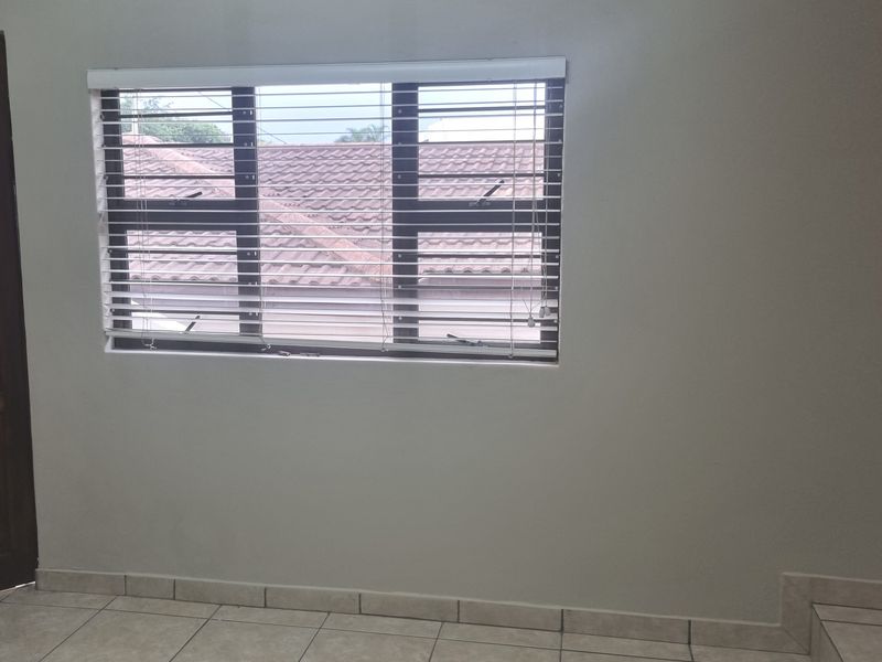 A clean, empty room featuring neutral tiled flooring and a window fitted with horizontal blinds, offering a blank canvas for interior design.