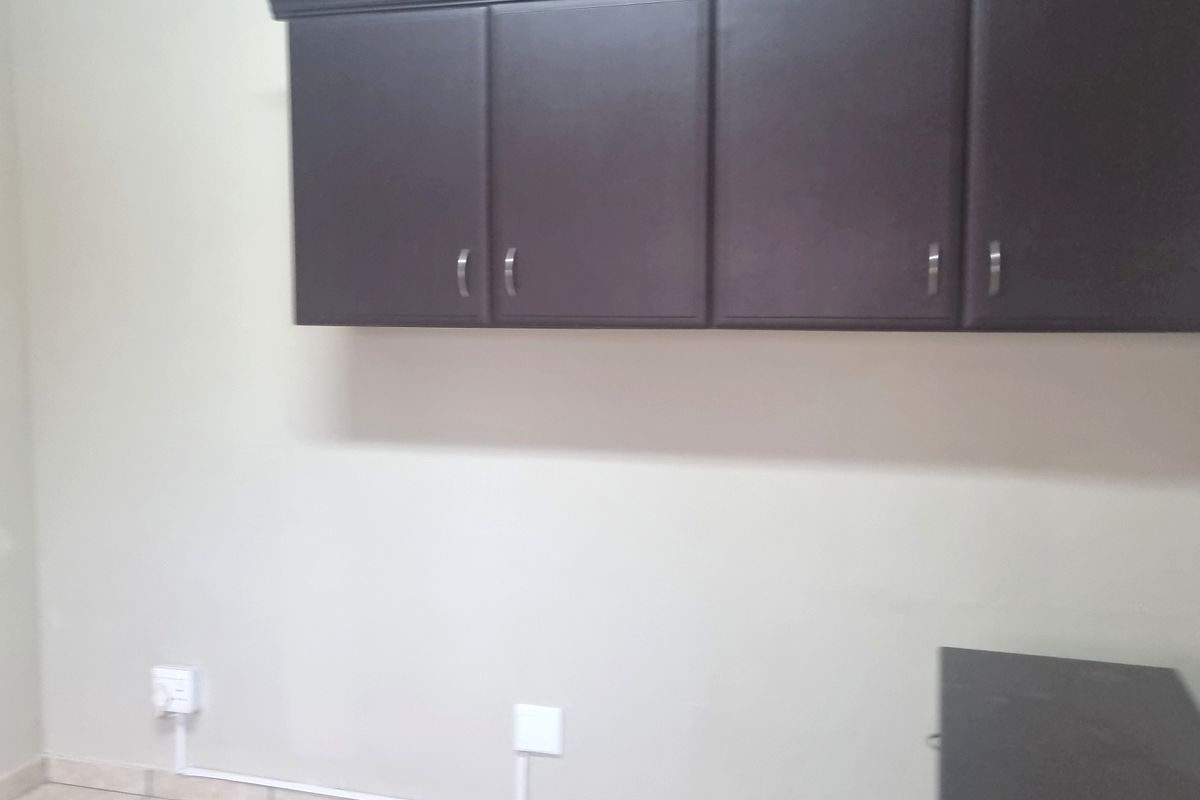 A utility space featuring tiled flooring, built-in overhead dark cabinetry, and a wall-mounted air conditioning unit with visible surface-mounted electrical wiring.