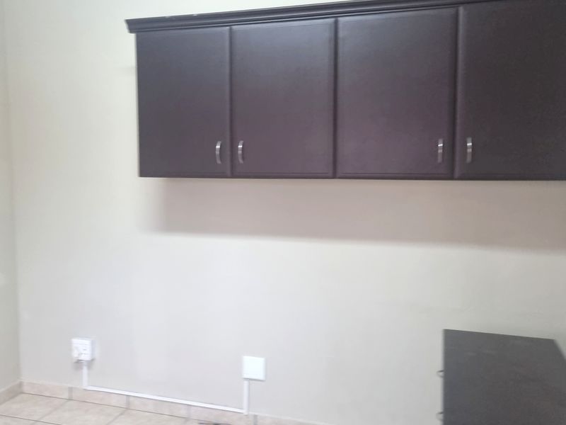 A utility space featuring tiled flooring, built-in overhead dark cabinetry, and a wall-mounted air conditioning unit with visible surface-mounted electrical wiring.