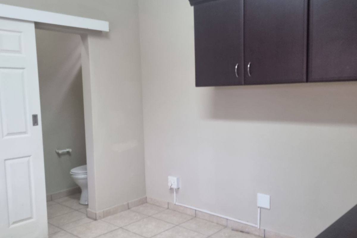 A functional kitchen area featuring dark wall-mounted cabinetry, tiled flooring, and an integrated air conditioning unit, with an adjacent bathroom visible through a sliding door.