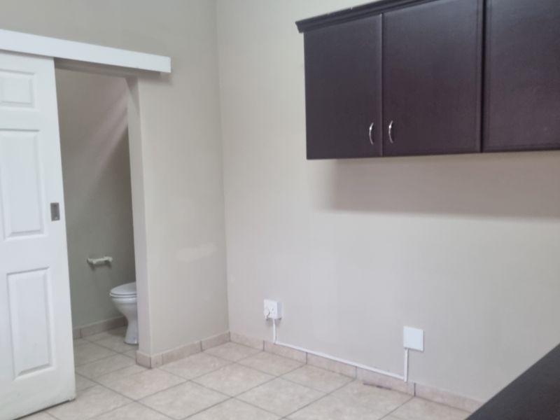 A functional kitchen area featuring dark wall-mounted cabinetry, tiled flooring, and an integrated air conditioning unit, with an adjacent bathroom visible through a sliding door.
