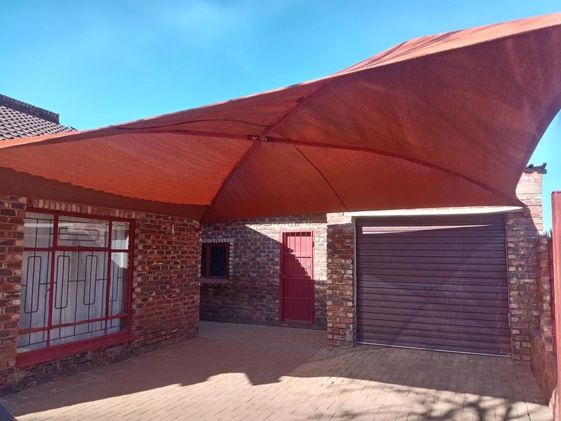 Front exterior view featuring a brick facade, paved driveway, secure garage door, and a large overhead shade sail structure.