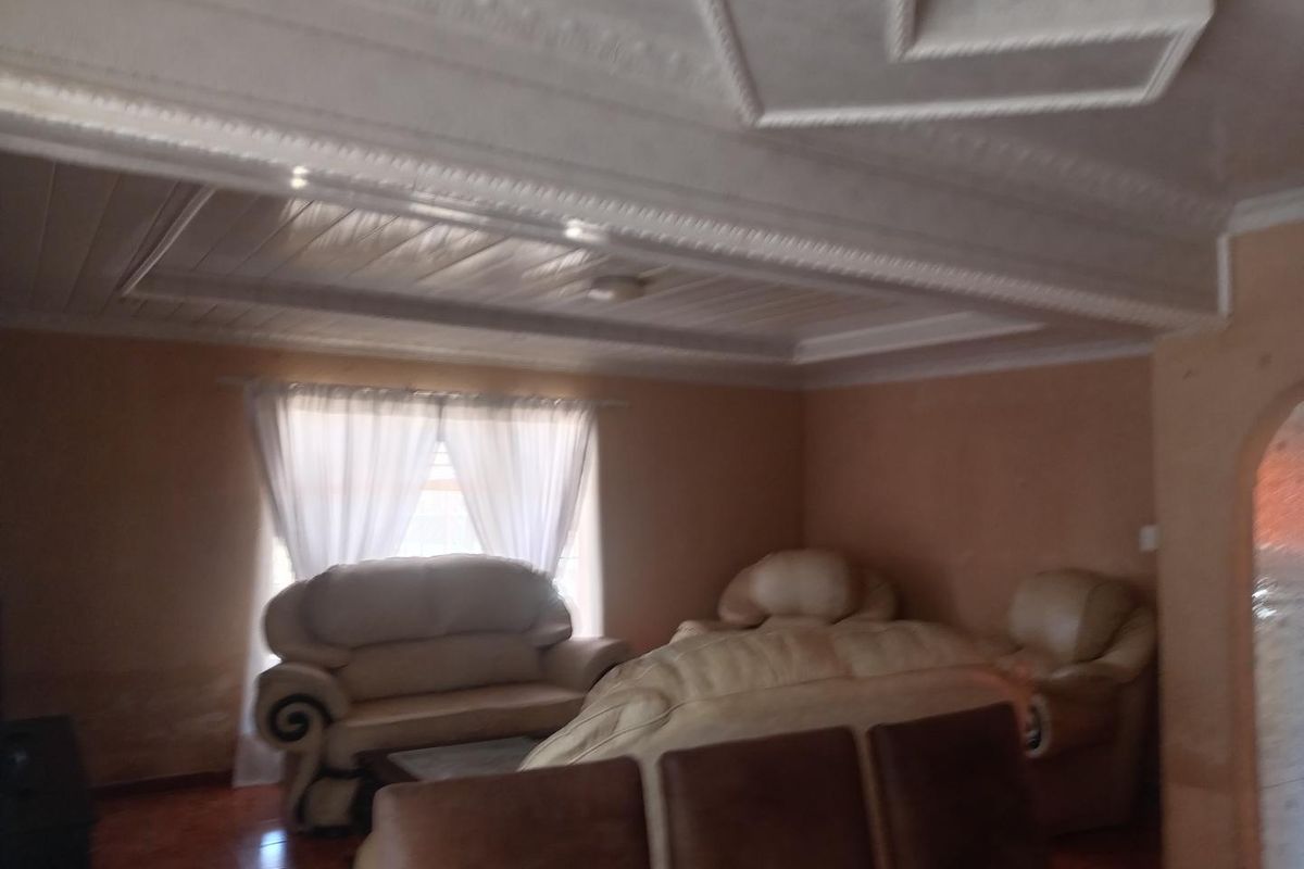 A living room featuring decorative ceiling molding and tiled flooring, currently showing signs of wall staining and dampness requiring maintenance.