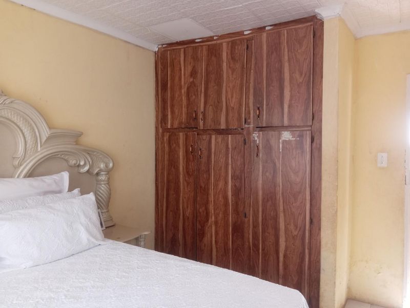 Bedroom featuring a large built-in wooden wardrobe and textured ceiling tiles, requiring cosmetic updates to improve the overall aesthetic.