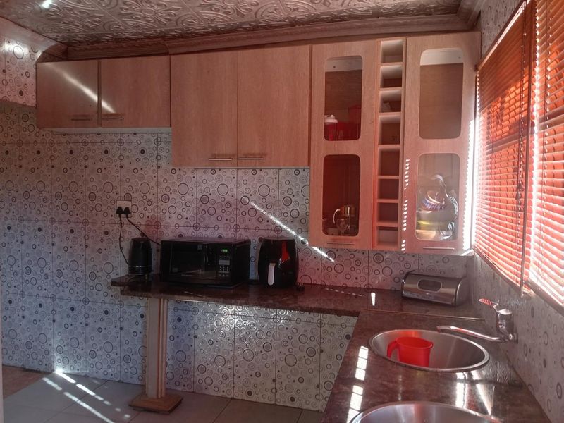 A functional kitchen featuring laminate cabinetry, granite countertops, double stainless steel sinks, and decorative ceiling tiles with a tiled backsplash.