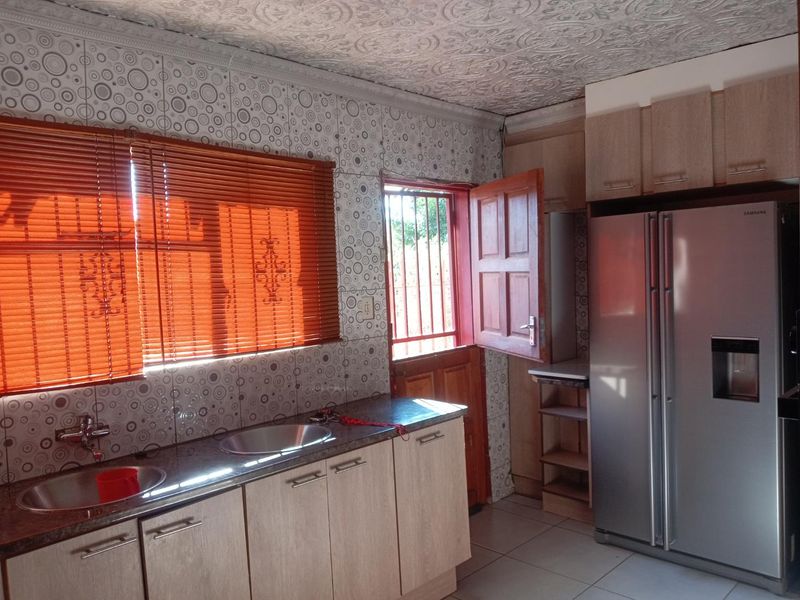 Kitchen featuring laminate cabinetry, granite countertops, double sink, and patterned wall tiles with direct access to the exterior via a security gate.