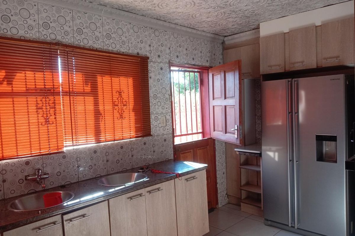 Kitchen featuring laminate cabinetry, granite countertops, double sink, and patterned wall tiles with direct access to the exterior via a security gate.