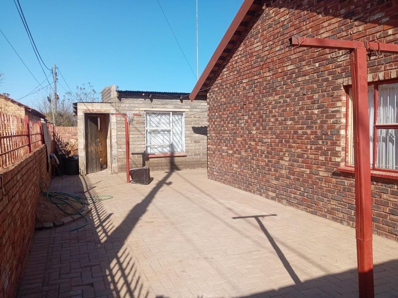 A paved rear courtyard featuring face brick exterior walls, a security-gated entrance, and a functional outdoor washing area.