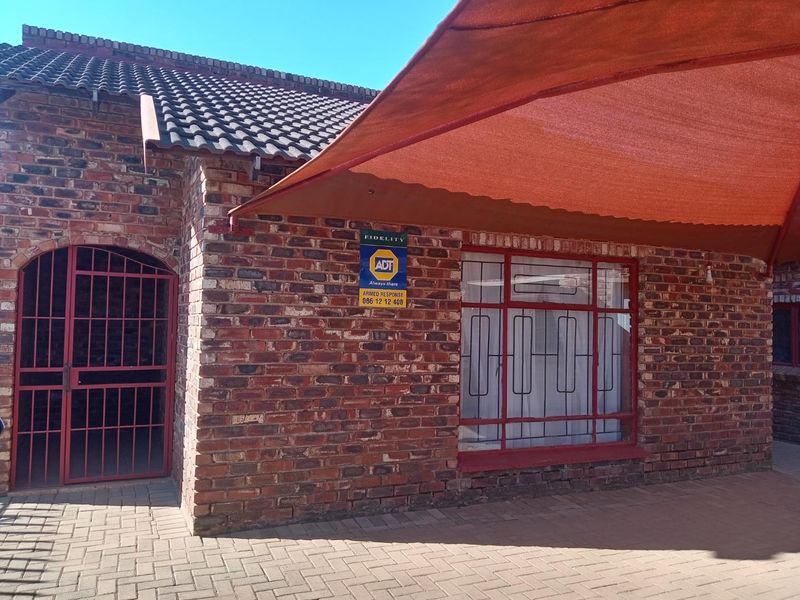 Front exterior view of a face brick house featuring a tiled roof, security gate, burglar bars, and a large shade sail over the paved area.
