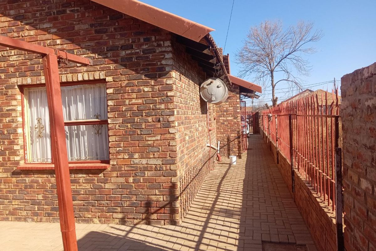 A side view of the property featuring face brick exterior walls, a paved walkway, and metal security fencing along the perimeter.