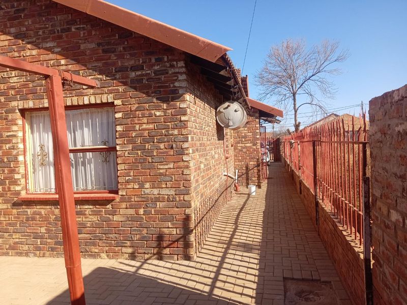 A side view of the property featuring face brick exterior walls, a paved walkway, and metal security fencing along the perimeter.