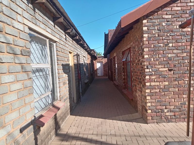 A narrow paved walkway between two face brick structures, featuring security-barred windows and simple roof overhangs.