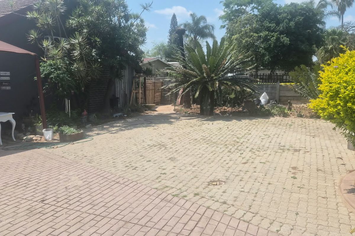 A rear exterior view featuring a paved driveway area, mature garden landscaping, and boundary walling.