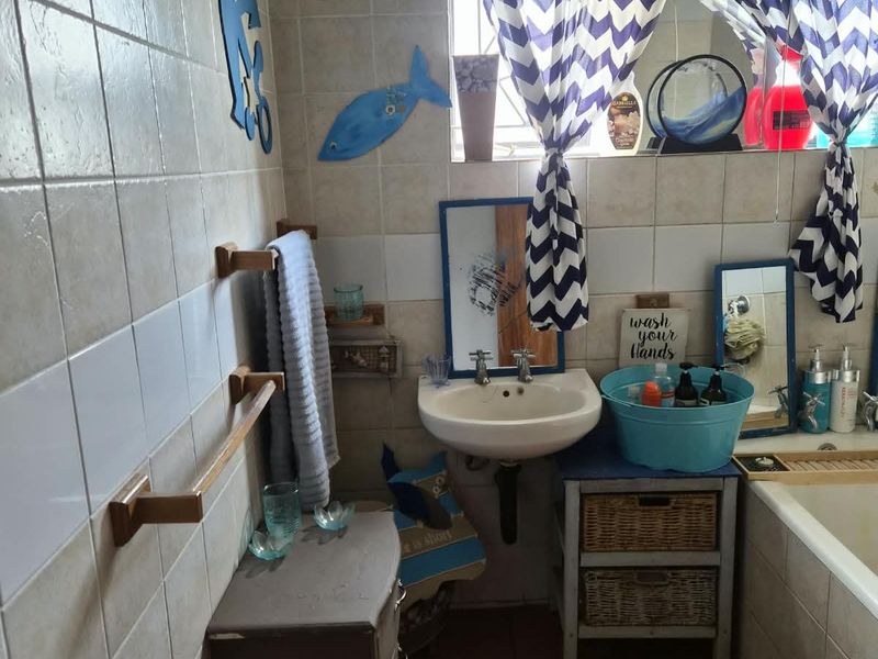A functional bathroom featuring a pedestal basin, bathtub, and tiled finishes, offering potential for a modern renovation to update the dated aesthetic.