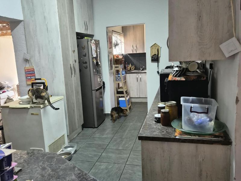 A functional kitchen featuring built-in cabinetry, laminate countertops, and tiled flooring, with an adjacent scullery area requiring some finishing touches.