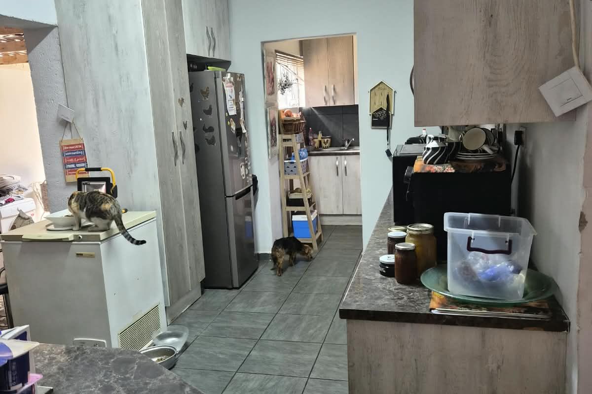 A functional kitchen featuring built-in cabinetry, laminate countertops, and tiled flooring, with an adjacent scullery area requiring some finishing touches.