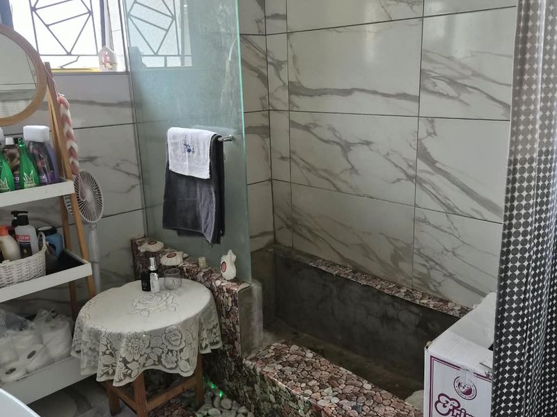 Bathroom featuring a custom raised shower area with stone cladding, glass screen, and marble-effect wall tiles.