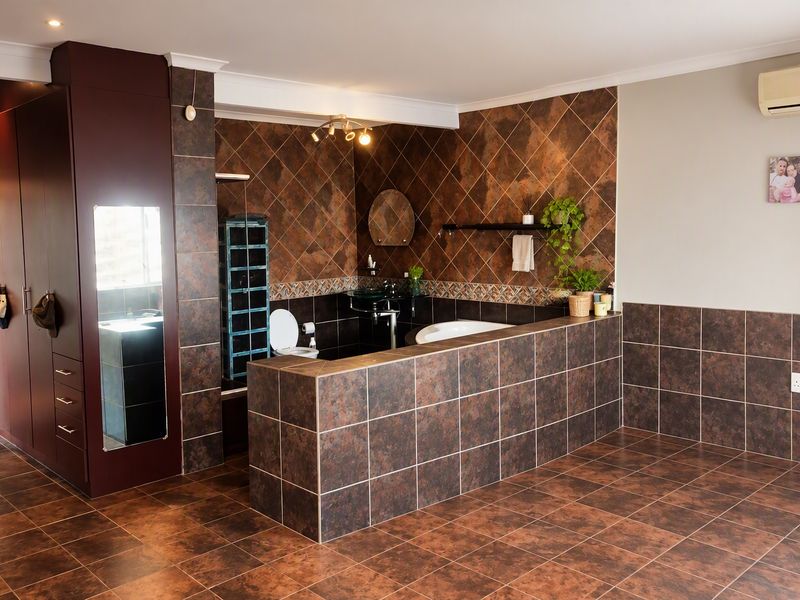 Spacious bathroom featuring dark brown tiled finishes, built-in cabinetry, a bathtub, and a wall-mounted air conditioning unit.