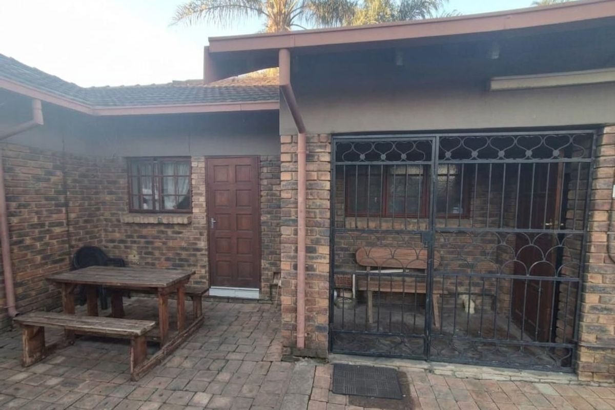 A rear exterior view of the house featuring face brick walls, a paved patio area, and a secure gated entrance.