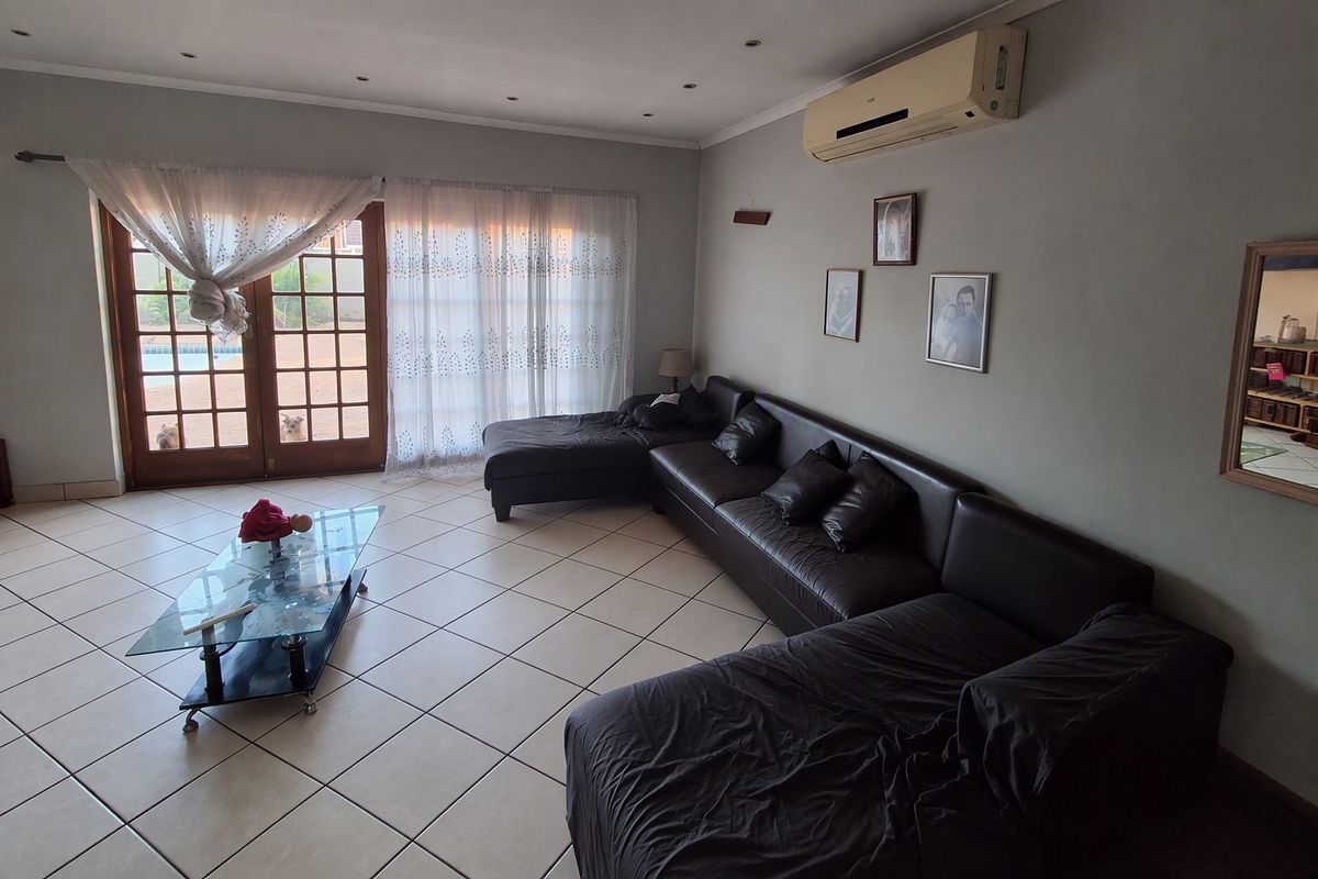 Spacious living room featuring tiled flooring, recessed lighting, and a wall-mounted air conditioning unit, with direct access to the outdoor area through glass doors.