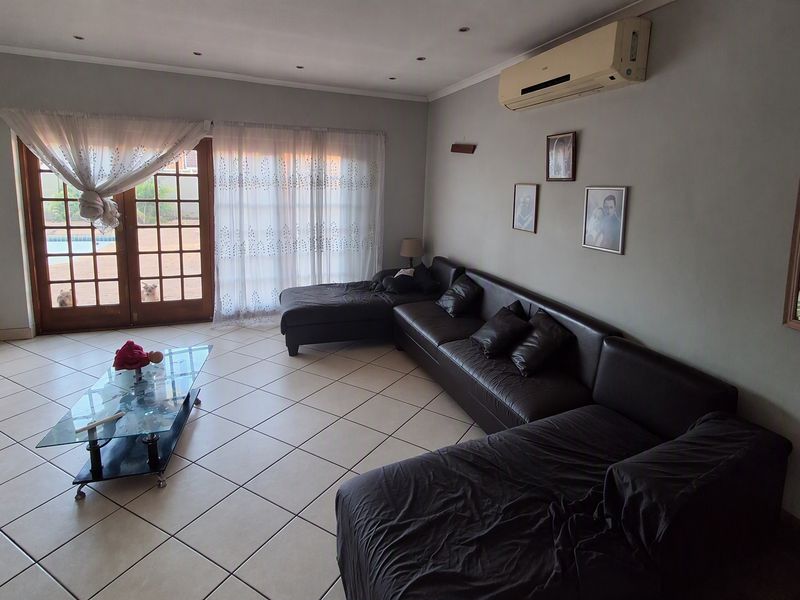 Spacious living room featuring tiled flooring, recessed lighting, and a wall-mounted air conditioning unit, with direct access to the outdoor area through glass doors.