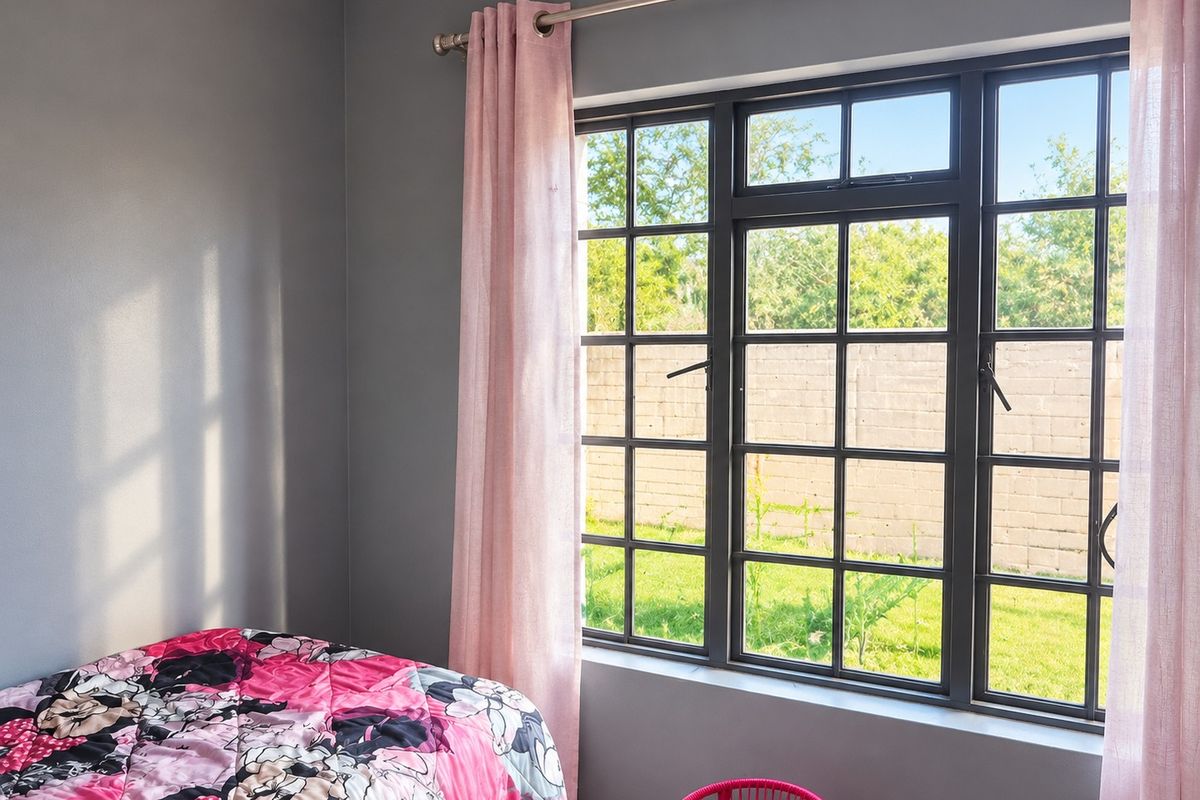 A bedroom featuring dark grey walls and large aluminium-framed windows that provide natural light and a view of the garden.