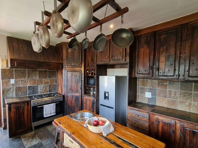 Rustic kitchen featuring dark wood cabinetry, stone tile backsplash, a central island with a sink, and a gas stove with an integrated extractor.
