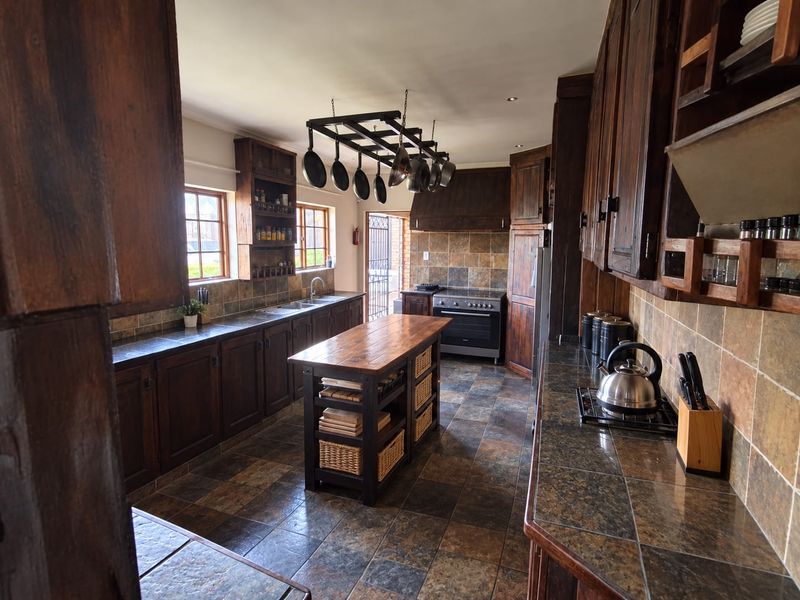 Spacious kitchen featuring dark wood cabinetry, stone tile countertops, a central island, and a hanging pot rack, offering a rustic and functional cooking space.