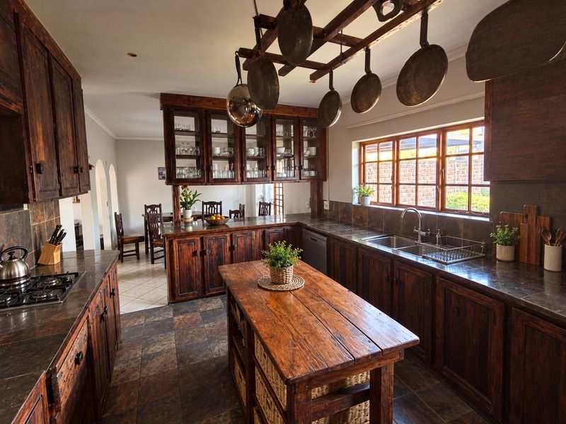 A rustic-style kitchen featuring dark wood cabinetry, stone countertops, a central island, and a built-in gas hob with an overhead pot rack.