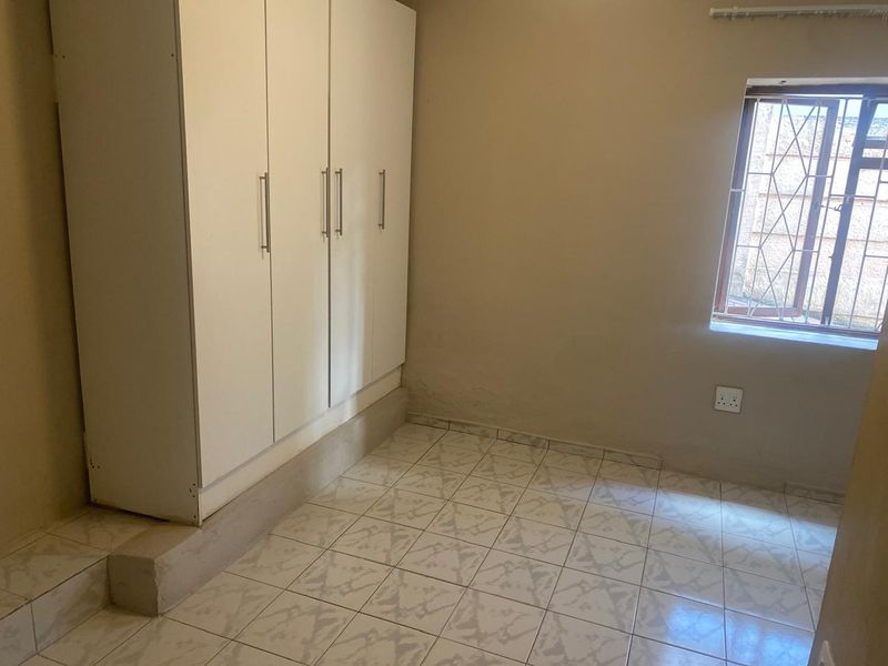 A compact bedroom featuring tiled flooring, a built-in wardrobe, and a window fitted with security bars.