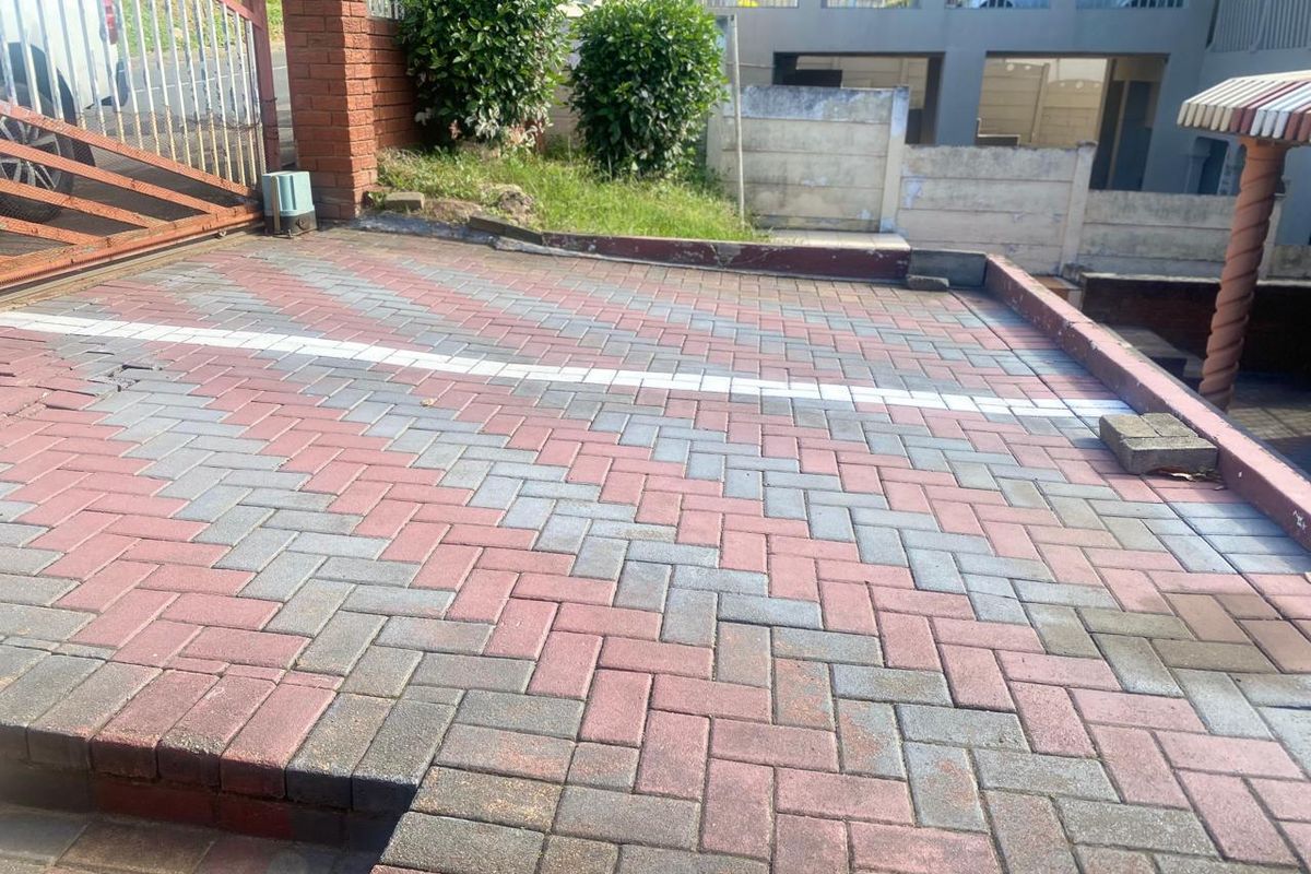 A paved front driveway area featuring brick boundary walls and a metal gate entrance.
