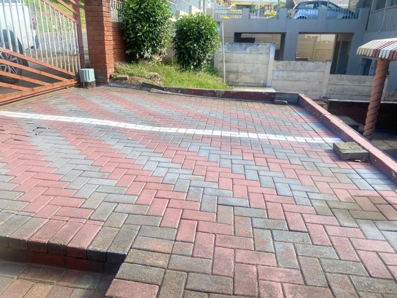A paved front driveway area featuring brick boundary walls and a metal gate entrance.