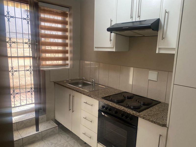 A compact, functional kitchen featuring white cabinetry, granite countertops, a built-in oven with electric hob, and direct access to an outdoor area.