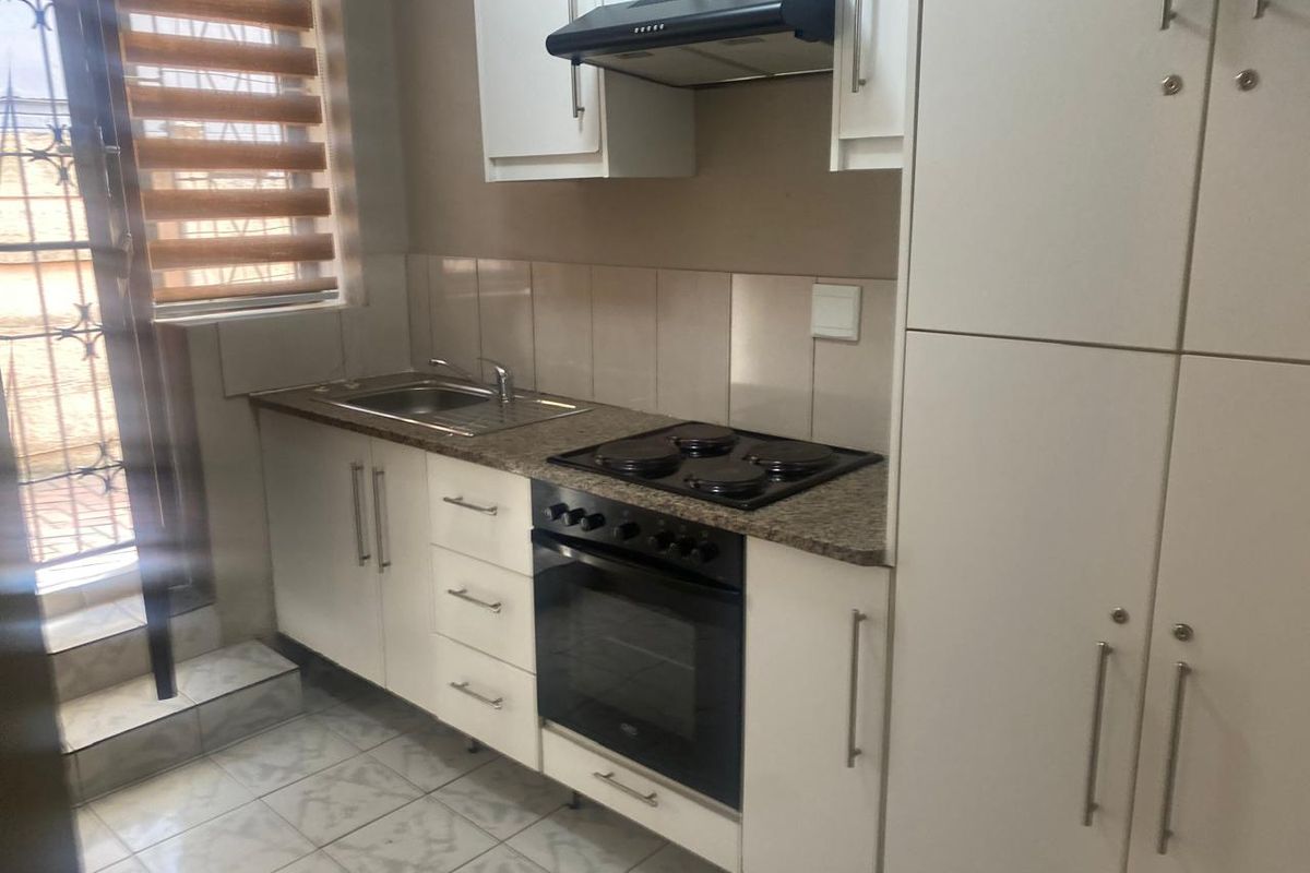 A compact, functional kitchen featuring white built-in cabinetry, granite countertops, a built-in oven with hob, and tiled flooring with direct access to an outdoor area.