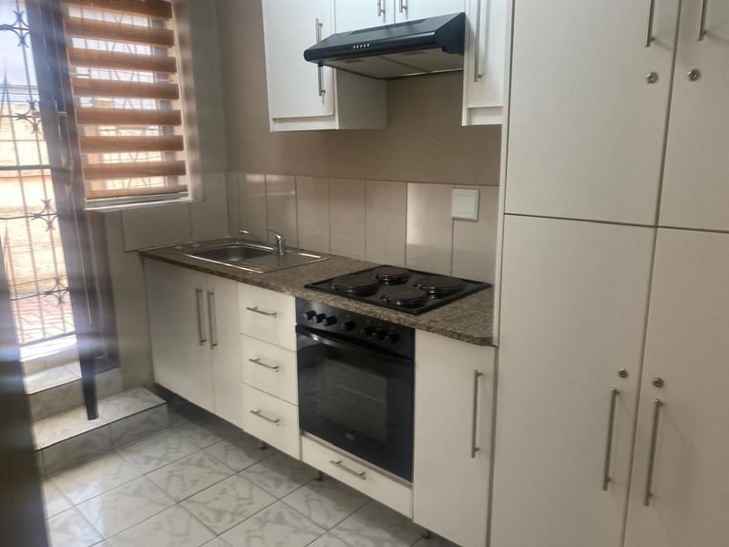 A compact, functional kitchen featuring white built-in cabinetry, granite countertops, a built-in oven with hob, and tiled flooring with direct access to an outdoor area.