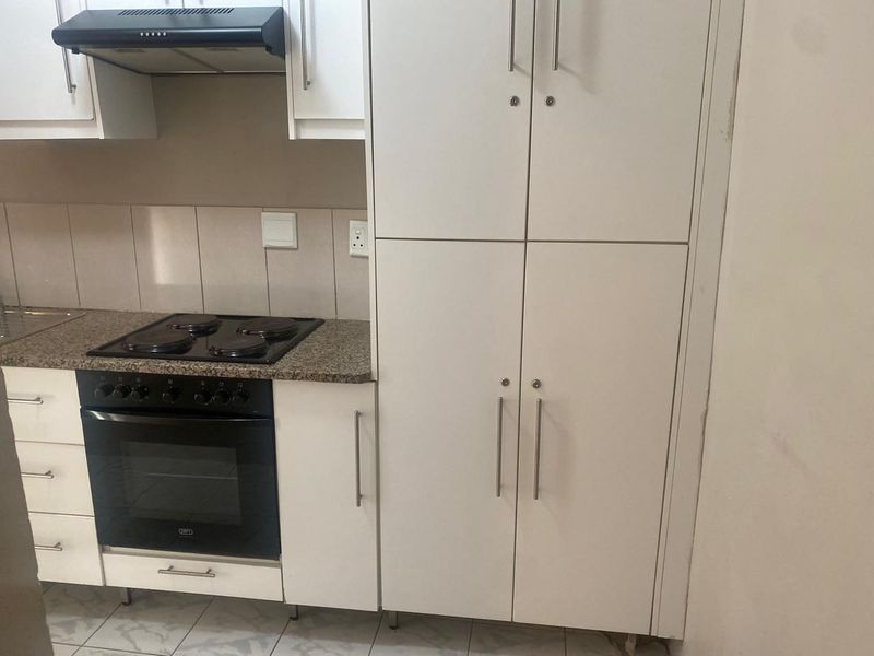 A functional kitchen featuring white built-in cabinetry, granite countertops, a built-in oven with electric hob, and an extractor fan.