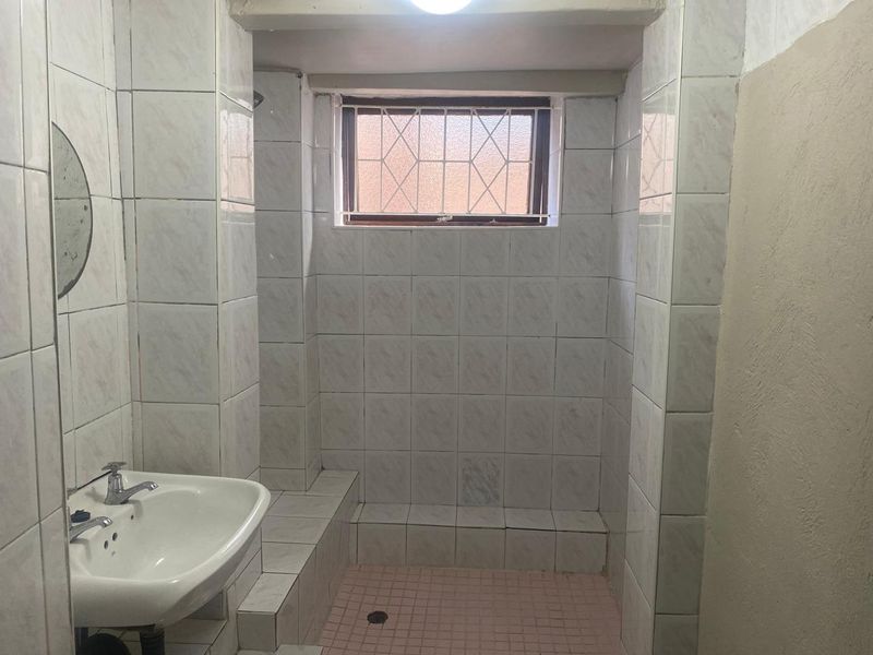 A functional bathroom featuring a pedestal basin and a tiled shower enclosure with a small window and security bars.