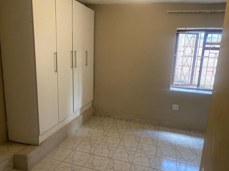 A compact bedroom featuring tiled flooring, a built-in wardrobe, and a window fitted with security bars.