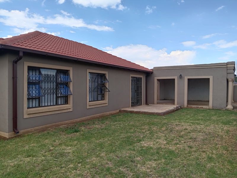 Rear view of the house featuring a tiled roof, plastered exterior walls, security bars on windows, and a paved patio area leading to the garden.